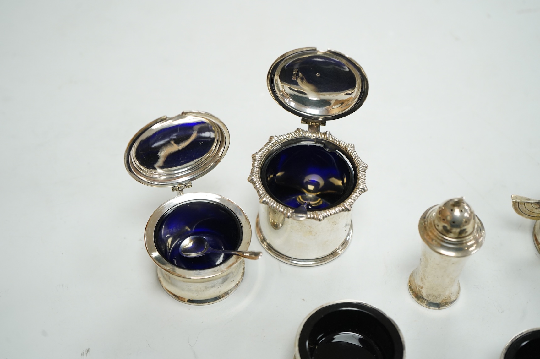 A George V Art Deco three piece silver condiment set and two spoons by William Adams Ltd, Birmingham, 1935, together with a pair of late Victorian pierced silver salts with blue glass liners and an Edwardian silver musta